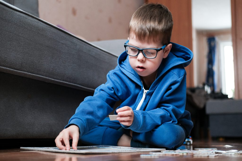 Junge mit Autismus sitzt auf dem Boden neben dem Sofa und puzzelt. 
